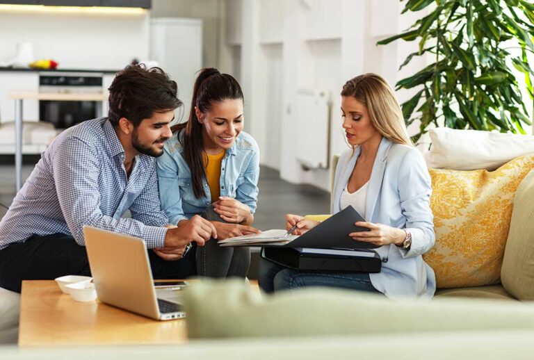 Older couple at a kitchen table reviewing paperwork and insurance documents together in a well-lit home.
